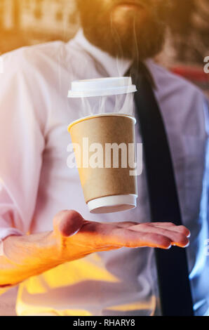 Barista in una camicia bianca con una cravatta detiene galleggianti in aria un bicchiere di carta con una bevanda calda sul suo le braccia tese. Barista concetto procedura guidata. Backgroun Foto Stock