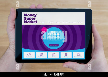 Un uomo guarda il sito web MoneySuperMarket sul suo iPad dispositivo tablet, sparato contro un tavolo di legno top sfondo (solo uso editoriale). Foto Stock