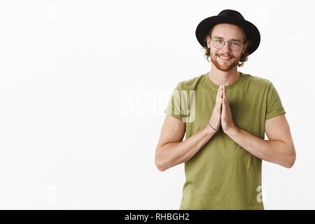 Guy rendendo angelo guardare come agiscono gli innocenti e carino per ricevere desiderabile. Bello affascinante biondo maschio in bicchieri e hat sorridente sincero come Foto Stock