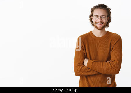Vita-up shot di amichevole-cercando felice unione maschio con i capelli lunghi e la barba in bicchieri e maglione, tenendo le mani incrociate sul corpo con Foto Stock