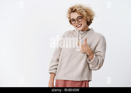 Hai fatto bene. Ritratto di gioiosa soddisfatto ed impressionato bella affascinante allegro biondo femmina in bicchieri e maglione che mostra il pollice in alto e Foto Stock