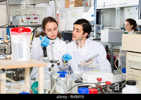 Due diligente positivo ai giovani scienziati che lavorano insieme nel laboratorio di scrittura di report sui risultati di esperimenti di chimica in notebook Foto Stock