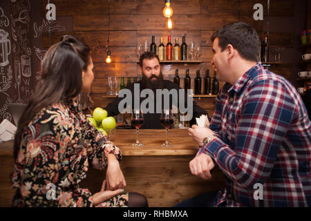 Bello il barista parlando con i clienti al bancone bar in un pub. Hipster pub. Foto Stock