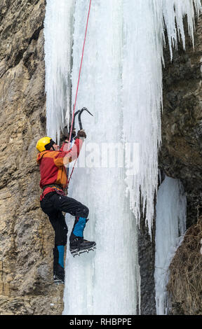 Extreme arrampicata su ghiaccio. L'uomo la scalata di cascate ghiacciate con piccozze e ramponi. Giallo casco alpina Foto Stock