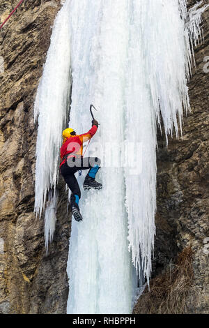 Extreme arrampicata su ghiaccio. L'uomo la scalata di cascate ghiacciate con piccozze e ramponi. Foto Stock