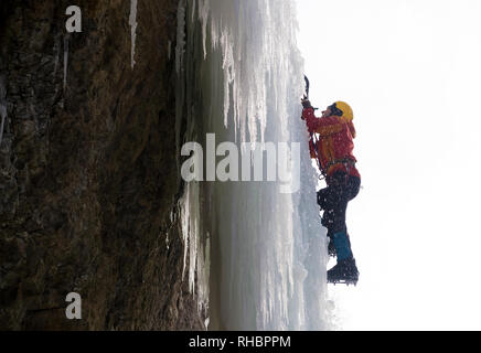 Extreme arrampicata su ghiaccio. L'uomo la scalata di cascate ghiacciate con piccozze e ramponi. Inverno Foto Stock