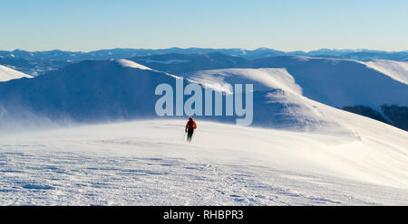 Solitarie passeggiate turistiche sulla montagna innevata gamma. Sullo sfondo di una catena montuosa. Un forte vento freddo Blow up di neve. Cielo sereno e soleggiato. L'inverno. U Foto Stock