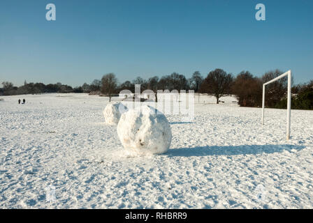 Snowballs enorme di fronte a un obiettivo aperto sulla coperta di neve sunny Hampstead Heath, giocare con il concetto di scala. Foto Stock