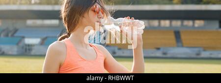 Giovane ragazza adolescente acqua potabile dalla bottiglia dopo aver acceso al stadium, panoramica banner sulla soleggiata sera primaverile. Foto Stock