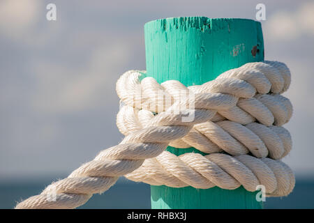 Bianco e spesso la corda avvolta sul legno verde post con il cielo e il mare in background Foto Stock