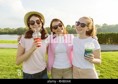 Ritratto di felice la madre e le figlie adolescenti di 14 e 16 anni, ragazze con bibite estive. Natura di sfondo, area ricreativa, Fiume Foto Stock