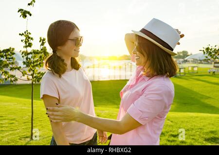 Comunicazione della capogruppo e adolescente, ragazza adolescente parlando con mom. Sfondo verde prato, la ricreazione e la zona di intrattenimento. Foto Stock