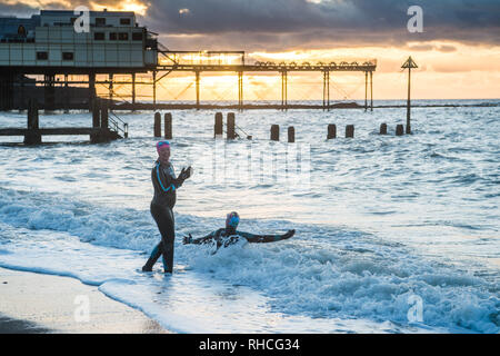 Aberystwyth Wales UK, sabato 02 febbraio 2019. Regno Unito: Meteo due donne hardy, in neoprene mute, andare per un tramonto nuotare nel mare in Aberystwyth nonostante la bitingly vento freddo ed il proseguimento del gelido e nevoso meteo che colpisce la maggior parte del Regno Unito thgis weeken Credito: keith morris/Alamy Live News Foto Stock