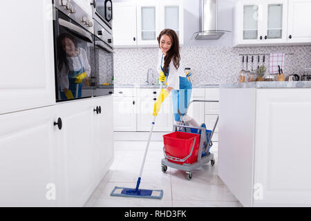 Felice bidello femmina piano di pulizia con Mop in cucina Foto Stock