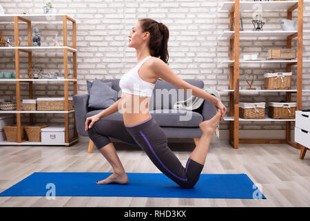 Vista laterale di una giovane donna in abbigliamento sportivo a praticare Yoga sul tappetino Fitness Foto Stock