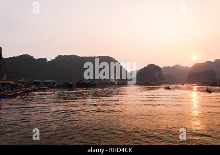 La gente del luogo in piccole casette di legno barca da pesca e villaggio di pescatori che si trova tra le pietre calcaree carsiche come il sole tramonta sulla baia di Ha Long, Vietnam Foto Stock