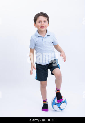 Bambino sorridente tenendo palla calcio. Poco il Calciatore con la palla. Isolato su bianco di sfondo per studio. Atleta maschio praticando sport olimpico gioco. Foto Stock