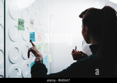 Silhouette di coworking persone per discutere idee durante la collaborazione sul progetto sharing soluzione creativa in piedi dietro la parete di vetro con note adesive Foto Stock