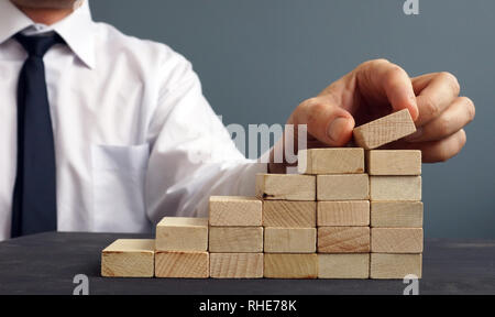 Il successo nel business e carriera. Uomo di figurine sorge su una scala da blocchi di legno. Raggiungimento. Foto Stock