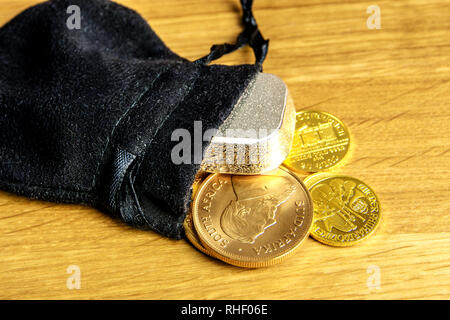 Primo piano delle monete in oro e argento mattone di cadere fuori moneybag nero e posa su sfondo di legno Foto Stock