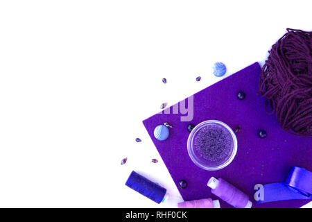 Un set di materiali per il ricamo in colore viola su uno sfondo bianco. Perle, filetti e lana per maglieria. Foto Stock