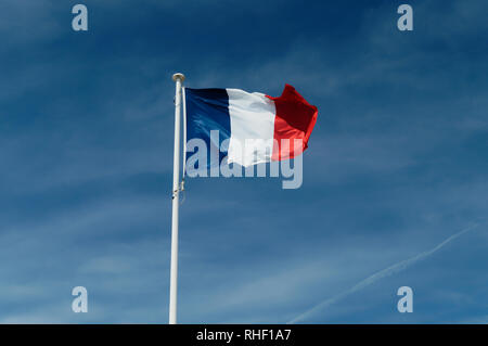 Bandiera francese nel vento contro un nuvoloso cielo blu sullo sfondo Foto Stock