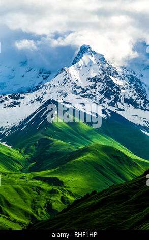 Bella vista della montagna innevata. Verdi campi e colline modifiche alla neve. Tempesta nuvole bianche sono visibili dietro gli illuminati di montagna. Somma Foto Stock