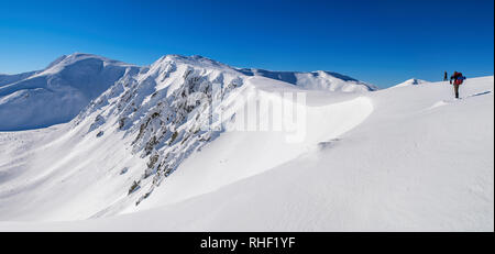 Panorama delle cime innevate. Rocce appuntite su un pendio ripido. Due turisti. Il cielo è chiaro, ben soleggiato. L'inverno. L'Ucraina Foto Stock