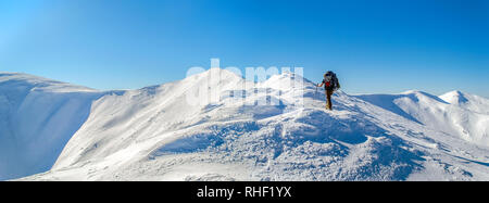 Tourist sorge alla sommità del crinale nevoso. Il cielo è chiaro, ben soleggiato. L'inverno. Ucraino Montagne dei Carpazi Foto Stock