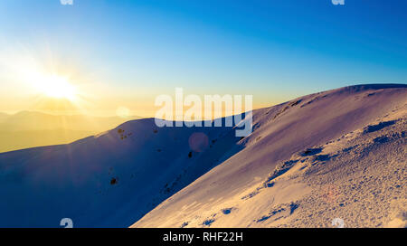 Tramonto in inverno le montagne innevate. La luce diretta del sole. Fascio di sun. La luce riflessa dalla neve. Cielo blu chiaro. Ombre profonde Foto Stock