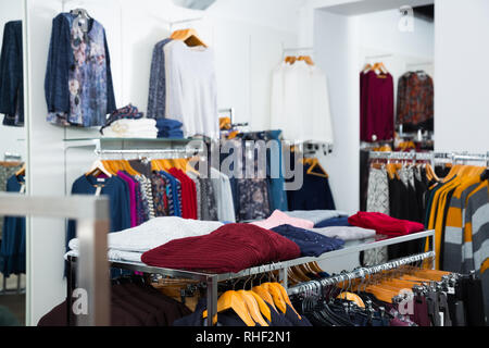 Interno del negozio di abbigliamento con le camicette e cardigan su grucce e piani di appoggio Foto Stock