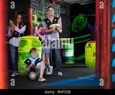 Ritratto di felici i bambini ed i loro genitori con le pistole laser durante il gioco lasertag in dark room Foto Stock