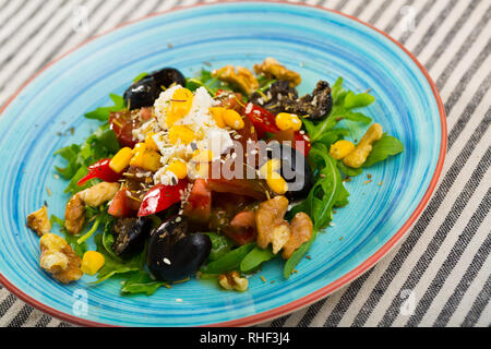 Vitamina insalata di rucola con pomodori, peperone rosso, il formaggio feta, noci e sesamo nella piastra su striped background tessile Foto Stock