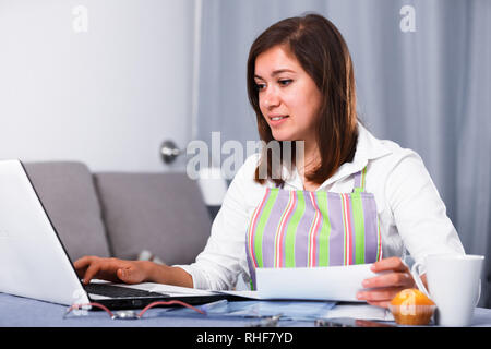 Giovane donna navigando attraverso utili suggerimenti per la cottura in Internet Foto Stock