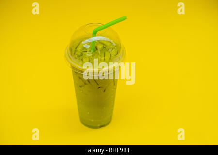 Il tè verde latte con il ghiaccio in una tazza di plastica e paglia su sfondo giallo. In casa Iced Matcha Latte Tè con latte take away Foto Stock