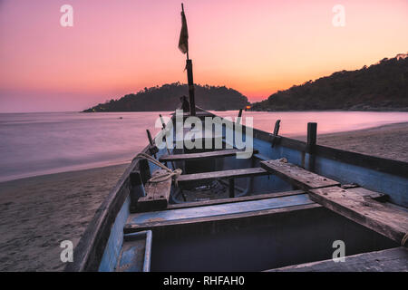 Sunset colorfull rosa e viola in una spiaggia tropicale di Goa in India con blu barca e isola Foto Stock