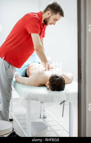 Giovane maschio terapista facendo massaggio alla schiena di un uomo disteso nel cabinet bianco della clinica di riabilitazione Foto Stock