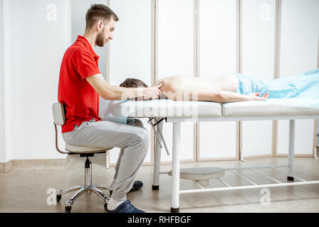 Giovane maschio terapista facendo massaggio alla schiena di un uomo disteso nel cabinet bianco della clinica di riabilitazione Foto Stock