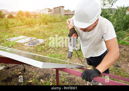 Close-up vista angolata del tecnico che sta lavorando con un cacciavite il collegamento di energia solare fotovoltaica in foto pannello esterno alla piattaforma di metallo. Alternativa ecologica rinnovabile sole verde fonti di energia concetto. Foto Stock