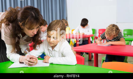 Gentile Maestro donna aiutando i bambini durante la lezione in classe Foto Stock