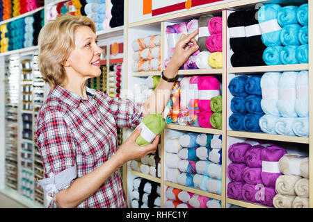 Coppia felice donna positiva di prelievo del cliente vari filati nel reparto di lavorazione a maglia Foto Stock