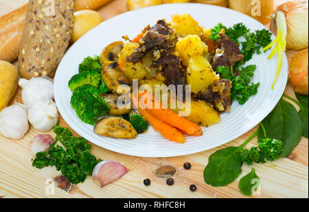 Gustoso stufato di manzo con patate servita con champignon fritto, cotto carote e broccoli Foto Stock