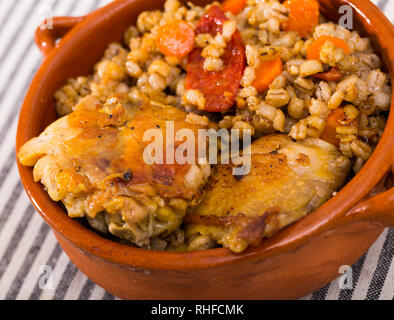 Cotto al forno cosce di pollo con orzo porridge nel recipiente di ceramica sulla tovaglia con striping Foto Stock