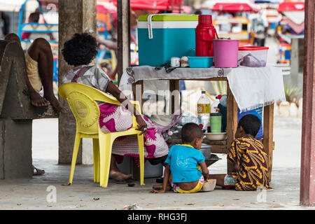 Toliara, Madagascar - Gennaio 10th, 2019: un malgascio madre con i suoi figli che la vendita di set di preparazione per tè e caffè con un tavolo di legno come contatore esterno in locale Foto Stock