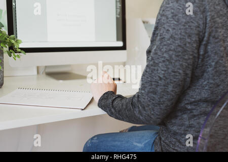 Donna in home office, dietro alla vista della donna anonima funzionante a una scrivania Foto Stock