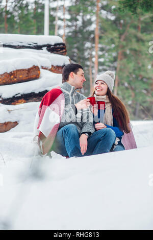 Sorridente giovane coppia con tazze di seduta in snow park. Bere bevande calde, divertendosi. Foto Stock
