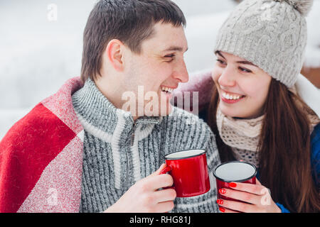 Sorridente giovane coppia con tazze di seduta in snow park. Bere bevande calde, divertendosi. Foto Stock