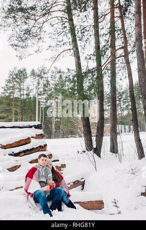 Sorridente giovane avvolto in un mantello e di bere il tè all'aperto nella foresta di inverno Foto Stock