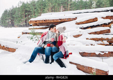 Sorridente giovane avvolto in un mantello e di bere il tè all'aperto nella foresta di inverno Foto Stock