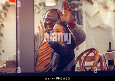 Padre e figlia sventolando pur vedendo la madre attraverso la finestra Foto Stock